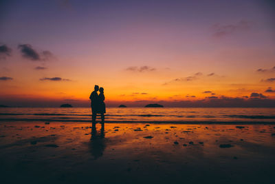 Couple standing on beach against sky during sunset