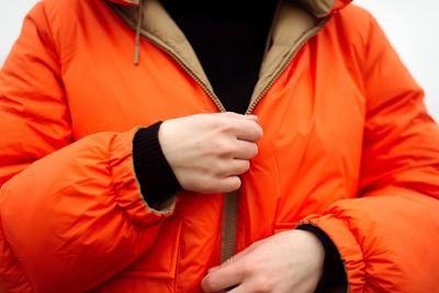 Unrecognizable female hands in bright orange jacket in winter