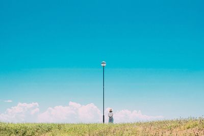 Rear view of woman standing on grassy field against blue sky during sunny day