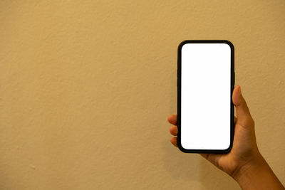 Cropped hand holding smart phone against yellow background
