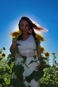 Portrait of smiling young woman on sunflower field against blue sky