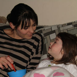 Mother feeding daughter resting on sofa at home