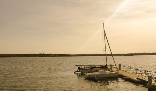 Sailboats moored on sea against sky during sunset