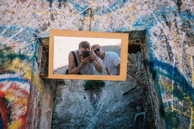 Reflection of people photographing through camera on mirror against wall