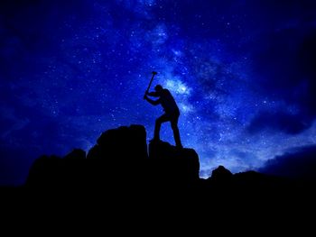 Silhouette man hammering rock against star field at night