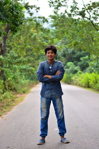 Full length portrait of young man standing on empty road against trees
