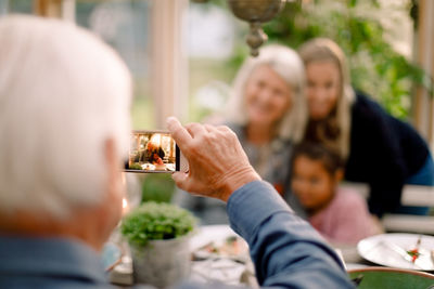 Senior man photographing happy family with mobile phone during lunch