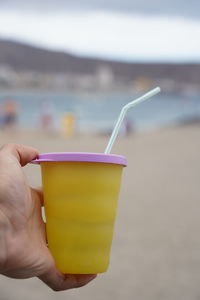 Holding plastic cup with drinking straw at beach