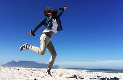 Woman jumping at beach against sky