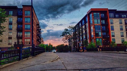 Road leading towards buildings against cloudy sky