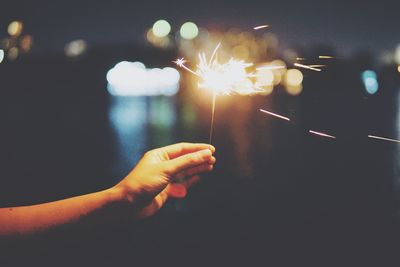 Cropped hand holding illuminated sparkler at night