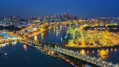 Illuminated bridge over river by buildings in city at night