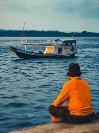 Rear view of man sitting on sea against sky