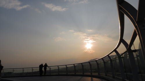 Man standing on railing by sea against sky