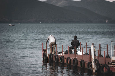 Rear view of men on pier by lake and mountains