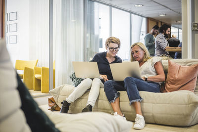 Full length of female entrepreneurs working over laptop while sitting on sofa in office