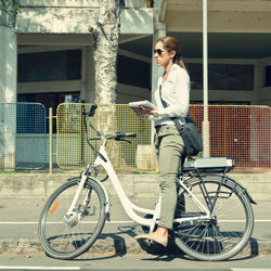 Side view of woman holding diary with bicycle standing on road