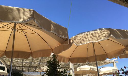 Low angle view of parasols against clear blue sky on sunny day