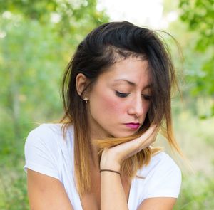 Thoughtful young woman with hand on chin against plants at field