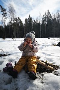 Portrait of 2-year-old sitting on tree stump and eating at snow covered field