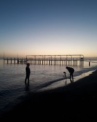 Silhouette people walking on beach against clear sky