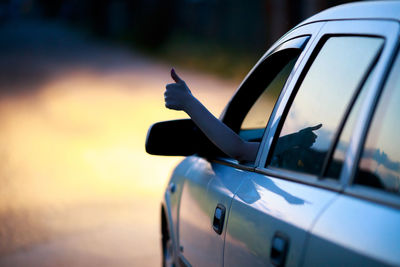 Cropped hand showing thumbs up from car on road