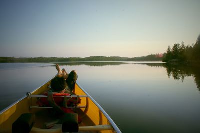 Men sitting on boat moored in lake against clear sky