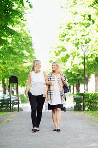 Full length of happy female friends communicating walking on garden path