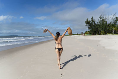 Woman in bikini walking on beach sand against blue sky. 