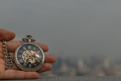 Close-up of hand holding clock against sea