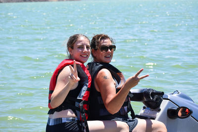 Portrait of smiling woman with daughter showing peace sign on jet boat