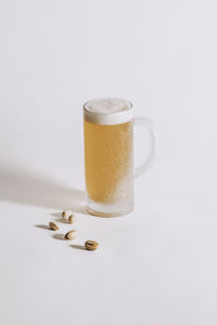 Chilled beer mug with frost on the surface and foam inside on a white background, pistachios