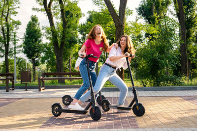 Three young girl friends on vacation having fun driving electric scooter through the city 