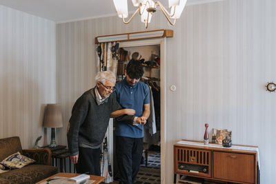 Male caregiver holding hands of senior man while walking at home