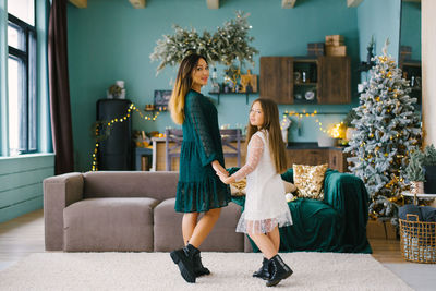 Mother and daughter holding hands in the living room of the house, decorated for christmas