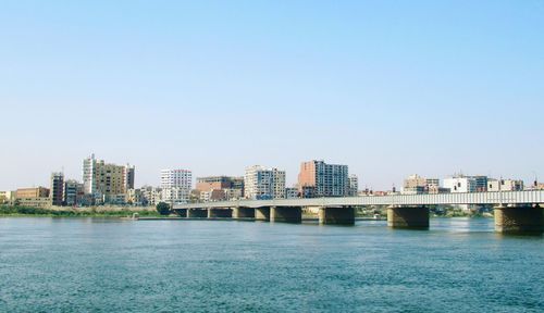 Scenic view of river by buildings against clear blue sky