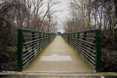 Footbridge amidst bare trees against sky