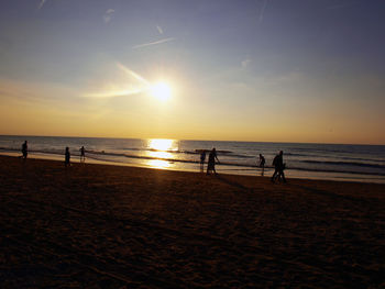 Silhouette people on beach against sky during sunset
