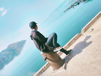 Man sitting on mountain by sea against sky