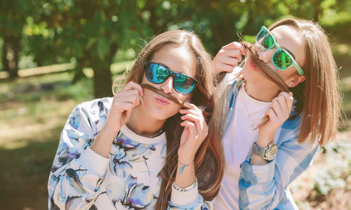 Portrait of friends wearing sunglasses while holding their hair as mustache at park