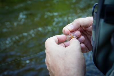 Cropped hand holding fishing tackle over river