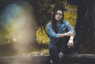 Portrait of young woman sitting on tree trunk in forest