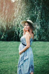 Portrait of pregnant woman touching abdomen while standing on grass