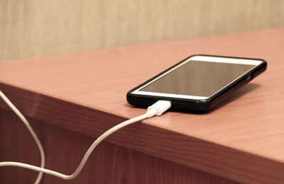 Close-up of smart phone being charged on wooden table