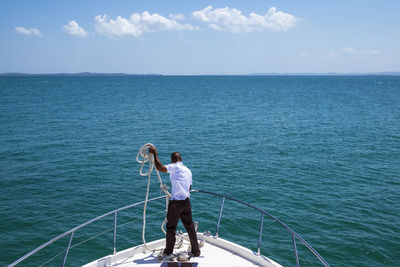 Rear view of man standing on railing against sea
