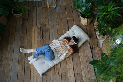 Shocked by vr young woman in virtual reality glasses watching 360 degree video lying on wooden floor