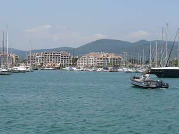 Boats moored at harbor by buildings against sky