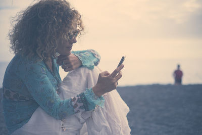 Side view of woman using phone at beach during sunset