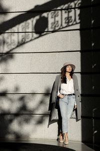 Full length portrait of woman standing against wall