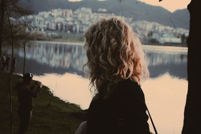 Rear view of woman standing by lake in city